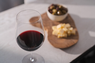 Red wine with olives and vintage cheese on white table