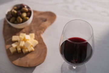 Red wine with olives and vintage cheese on white table