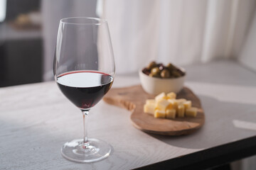 Red wine with olives and vintage cheese on white table