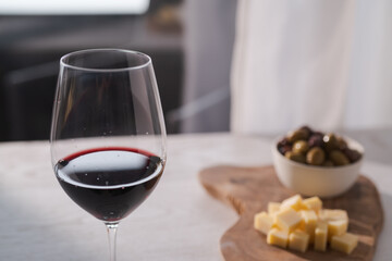 Red wine with olives and vintage cheese on white table
