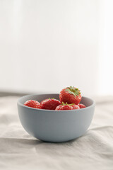 Organic ripe strawberries in blue ceramic bowl on white linen cloth