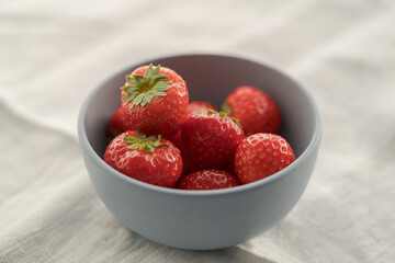 Organic ripe strawberries in blue ceramic bowl on white linen cloth