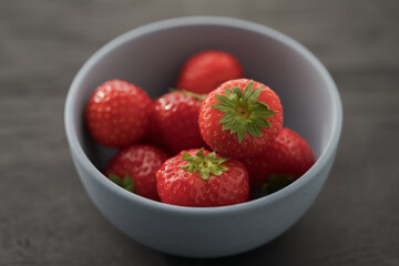 Organic ripe strawberries in blue ceramic bowl on black oak table