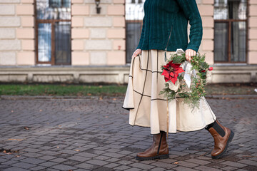 Fototapeta na wymiar Christmas wreath in the hands of a stylish woman, city walk.