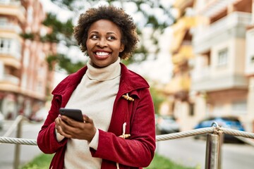 Beautiful business african american woman with afro hair smiling happy and confident outdoors at the city using smarpthone