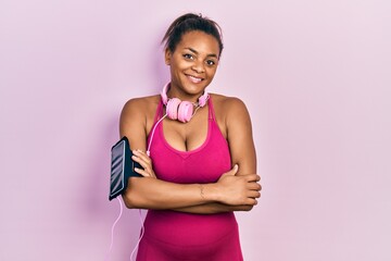 Young african american girl wearing gym clothes and using headphones happy face smiling with crossed arms looking at the camera. positive person.