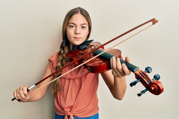 Beautiful brunette little girl playing violin relaxed with serious expression on face. simple and natural looking at the camera.