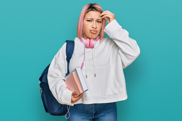 Hispanic woman with pink hair wearing student backpack and headphones worried and stressed about a problem with hand on forehead, nervous and anxious for crisis