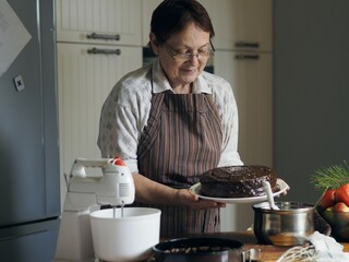 An elderly woman in the kitchen makes a cake. Healthy homemade food.