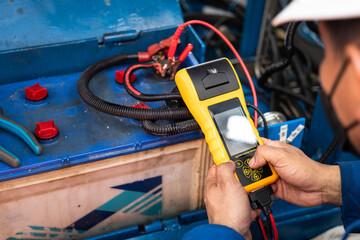 Action of a mechanic is using battery system tester device to testing electricity voltage of automotive batter. Industrial service action photo. Close-up and selective focus at people's hand.