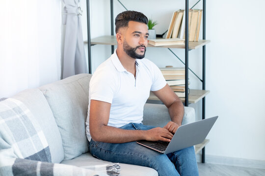 Freelance work. Arabian man. Virtual connection. Handsome thoughtful guy casual look sitting on sofa with laptop light room interior.