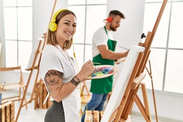 Young caucasian couple smiling happy listening to music and drawing at art studio.