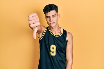 Young hispanic man wearing basketball uniform looking unhappy and angry showing rejection and negative with thumbs down gesture. bad expression.