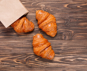 Top view of three croissants in a craft bag on a wooden background.
