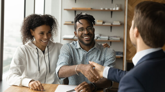 Happy African American family couple shaking hands with professional real estate agent broker lawyer financial advisor, thanking for professional consultation, celebrating making deal in office.