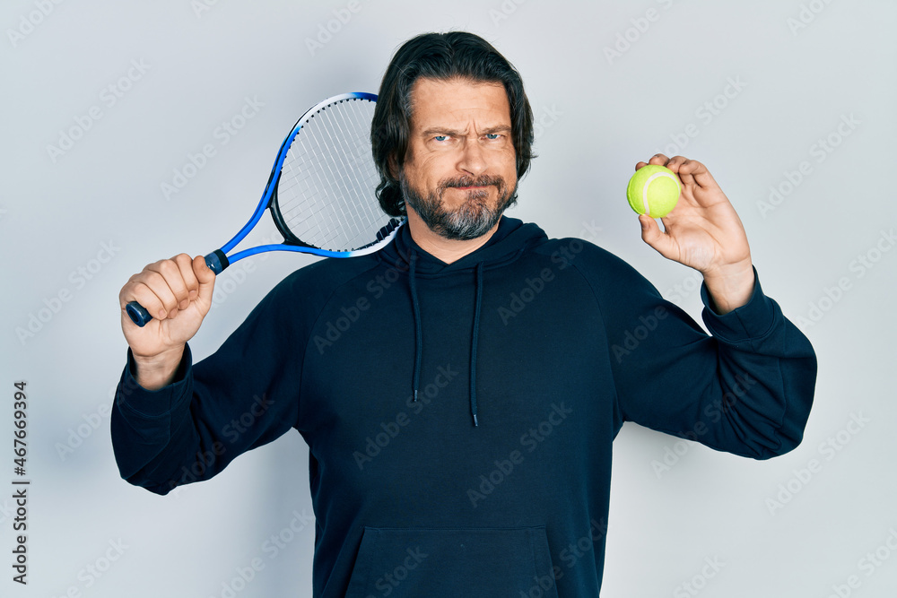 Sticker middle age caucasian man playing tennis holding racket and ball skeptic and nervous, frowning upset 