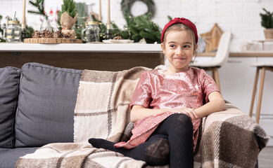 Funny little girl in a shiny pink dress in a home decor decorated for Christmas.