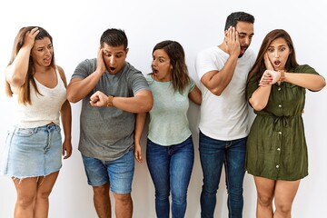 Group of young hispanic friends standing together over isolated background looking at the watch...