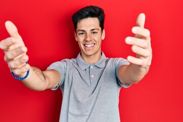 Young hispanic man wearing casual clothes looking at the camera smiling with open arms for hug. cheerful expression embracing happiness.