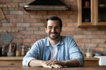 Portrait of happy confident young handsome bearded man wear glasses in casual clothes sit at table...