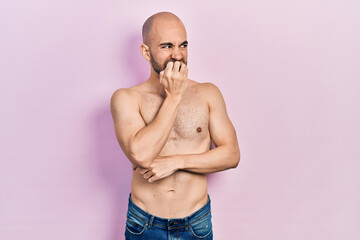 Young bald man standing shirtless looking stressed and nervous with hands on mouth biting nails. anxiety problem.