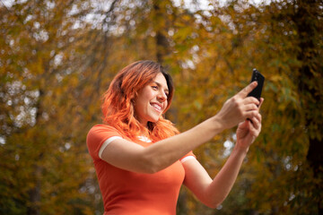 happy red-haired woman with cell phone in hand in a park in autumn