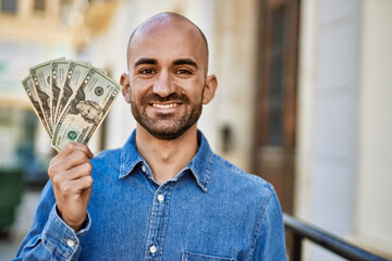 Young hispanic man smiling happy holding dollars at the city.