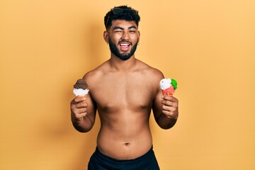 Arab man with beard wearing swimwear eating two ice cream cones winking looking at the camera with...