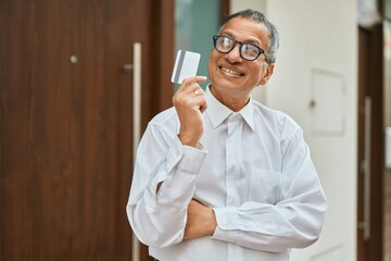 Middle age southeast asian man standing and smiling confident holding credit card by house entrance