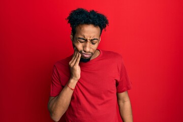 Fototapeta na wymiar Young african american man with beard wearing casual red t shirt touching mouth with hand with painful expression because of toothache or dental illness on teeth. dentist