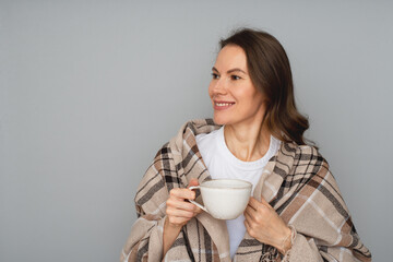 Brunette woman 39 old with cup of drink and wrap up in blanket, studio portrait