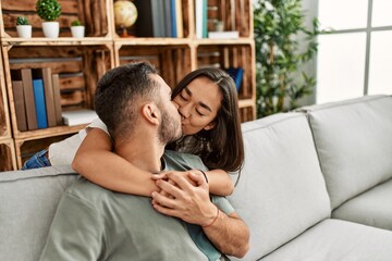 Young latin couple sitting on the sofa hugging and kissing at home.