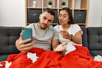 Young latin ill couple having medical teleconsultation using smartphone at home.