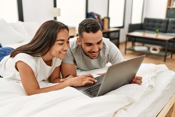 Young latin couple smiling happy using laptop lying on the bed.