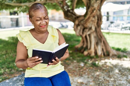 Senior african american woman reading book sitting on the bench at the park.