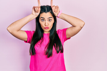 Fototapeta na wymiar Young hispanic girl wearing casual pink t shirt doing funny gesture with finger over head as bull horns