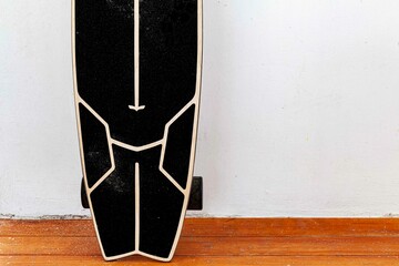 A black skateboard is placed on a white cement wall.