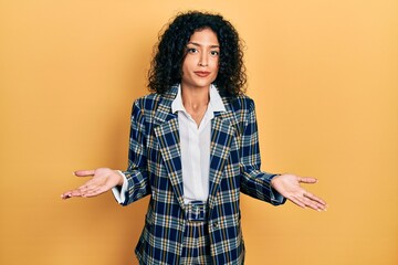 Young latin girl wearing business clothes clueless and confused expression with arms and hands...