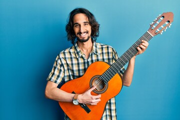 Young hispanic man playing classical guitar smiling with a happy and cool smile on face. showing teeth.