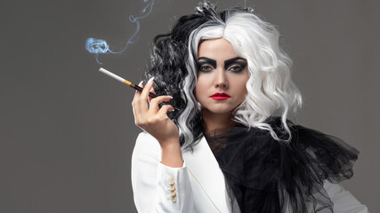 A fatal beauty in a daring fashion image with black and white hair. A rebellious stylish image for Halloween. a young woman in a black and white outfit smokes a cigarette using a mouthpiece