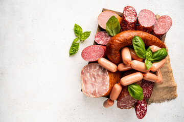 Set of different types of sausages, salami and smoked meat with basil in a box on white background....