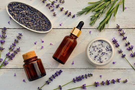 Lavender oil in a bottle, bath salt and lavender flowers on white wooden  background top view