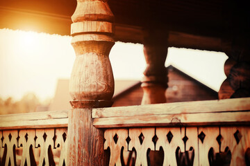 The veranda of the rustic wooden hut is decorated with carved railings and balustrades illuminated by sunlight. Wooden traditional decor in a Slavic village. Carpentry.