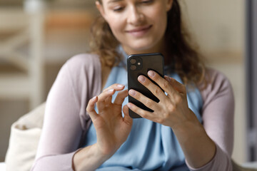 Fototapeta premium Close up relaxed pleased millennial woman using smartphone gadget, typing message communicating in social network, using online dating application, playing mobile game, web surfing information.