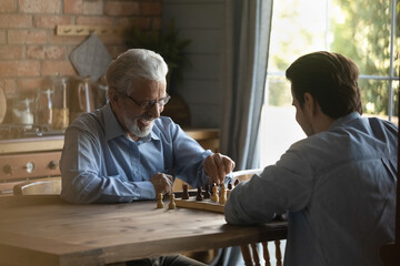 Battle at chessboard. Enthusiastic old father play friendly chess match at home with grownup son....