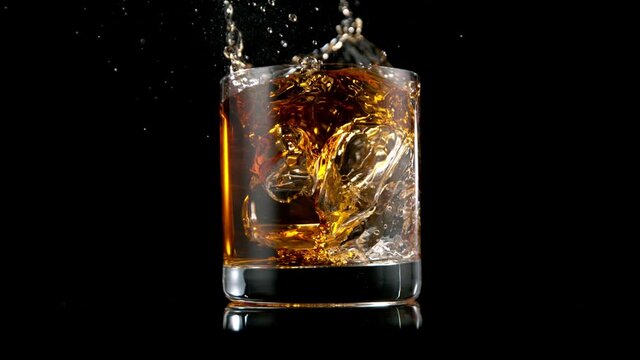 Super slow motion of falling ice cube into whiskey drink. Speed ramp effect. Filmed on high speed cinema camera.