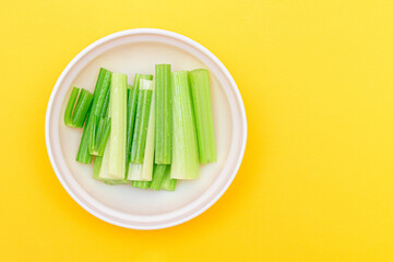 Fresh Chopped Celery Sticks with Water Drops in White Bowl on Yellow Background - Top View. Vegan and Vegetarian Culture. Raw Food. Healthy Diet with Negative Calorie Content