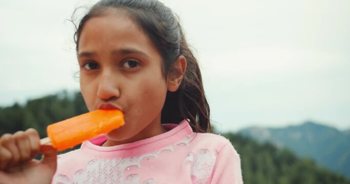 A South Asian girl eating a lollipop ice cream outdoors
