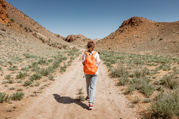 A woman with a backpack walks along a trail in a deserted canyon with red rocks. Hiking path and the dangers of solo trekking