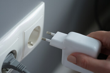 Hands plugging the charger into an outlet in the wall, close-up